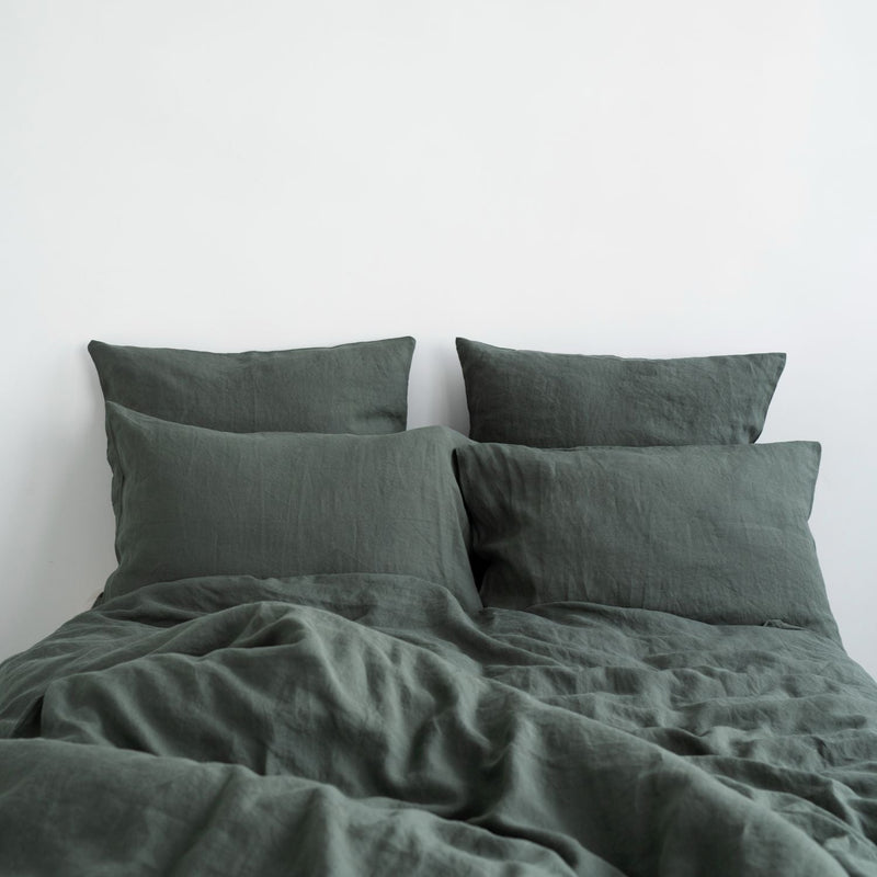Forest green linen bedding on a natural, unmade bed
